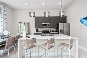 A modern kitchen with a central island, stainless steel appliances, and pendant lighting. - Beautiful Condo with Private Terrace Near Attractions (Kissimmee)