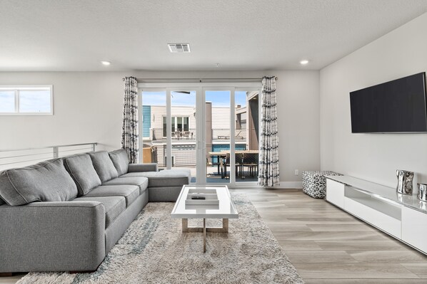 A modern living room with a sectional sofa, a coffee table, and a flat-screen TV mounted on the wall. - Beautiful Condo with Private Terrace Near Attractions (Kissimmee)