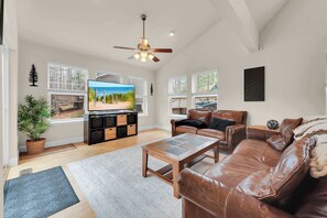 A spacious living room with a leather sofa, a coffee table, a TV, and a ceiling fan.