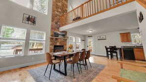 A spacious dining area with a stone fireplace, large windows, and a wooden staircase. - Stonewood Retreat AC, Firepit, Pool Tble, Masthope (Lackawaxen)