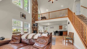 A spacious living room with a leather sofa, wooden staircase, and a dining area. - Stonewood Retreat AC, Firepit, Pool Tble, Masthope (Lackawaxen)