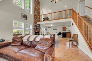 A spacious living room with a leather sofa, wooden staircase, and a dining area.