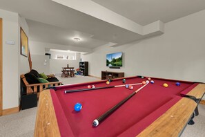 A pool table in a room with a sofa, a TV, and a bookshelf.