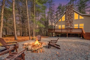 A cabin with a stone fireplace, outdoor seating, and a deck overlooking a forest.