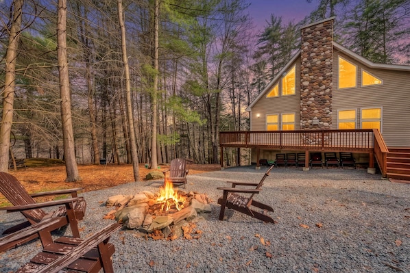 Eine Holzhütte mit Kamin aus Stein, Sitzgelegenheit im Freien und einer Terrasse mit Blick auf einen Wald.