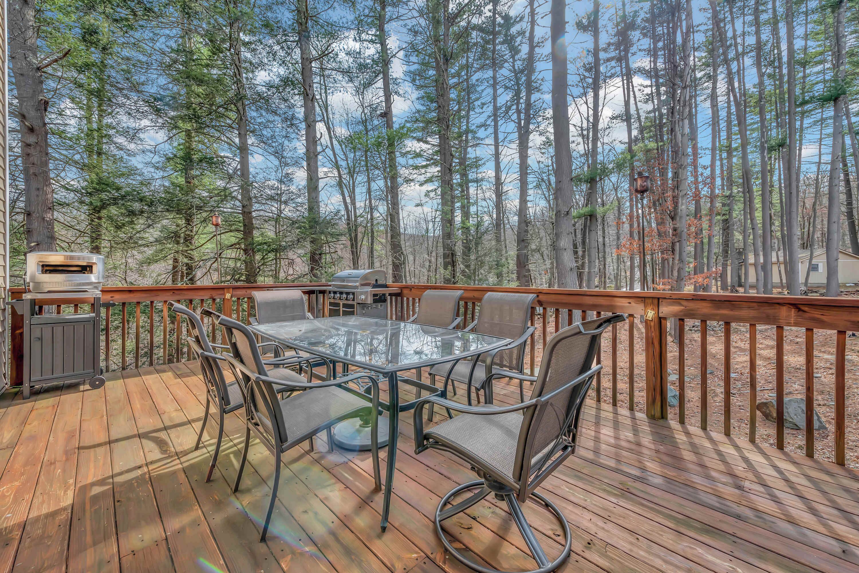 A deck with a glass-top table and chairs, surrounded by a wooden railing, overlooking a forested area.