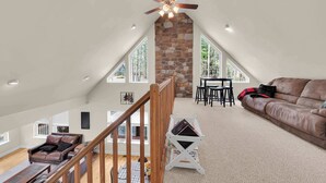 A spacious loft with a high ceiling, a stone fireplace, a wooden staircase, a leather sofa, and a dining area. - Stonewood Retreat AC, Firepit, Pool Tble, Masthope (Lackawaxen)