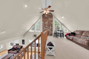 Ein geräumiger Dachboden mit hoher Decke, einem Steinkamin, einer Holztreppe, einem Ledersofa und einem Essbereich.
