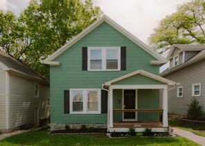 A two-story house with a green exterior, a front porch with a railing, and a small front yard. - Plaza Social - Steps from KC Street Car (Kansas City)
