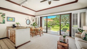 A spacious living area with a kitchen, dining table, and a sliding glass door leading to a garden. - Kiahuna Plantation Resort 58 Royal Garden 1 BD (Koloa)
