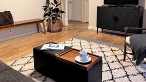 Una sala moderna con televisor de pantalla plana, una mesa de centro de madera con una bandeja, un sofá, un tapete estampado y una planta en maceta.