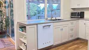 Una cocina moderna con armarios blancos, lavavajillas integrado, un lavamanos de acero inoxidable y un microondas.