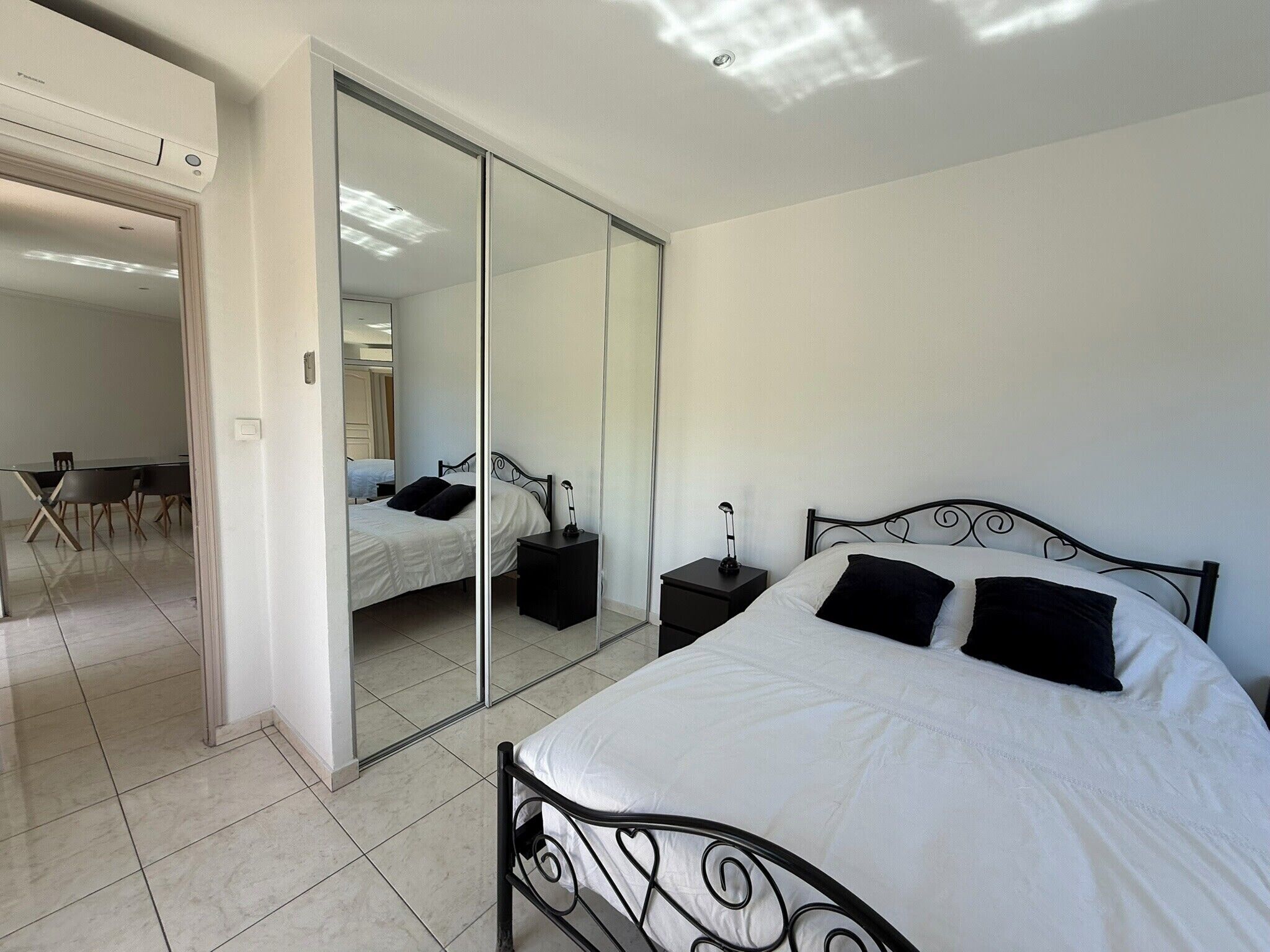 Une chambre à coucher comprenant un lit, une table de chevet, un miroir et une porte donnant sur une salle de bain.