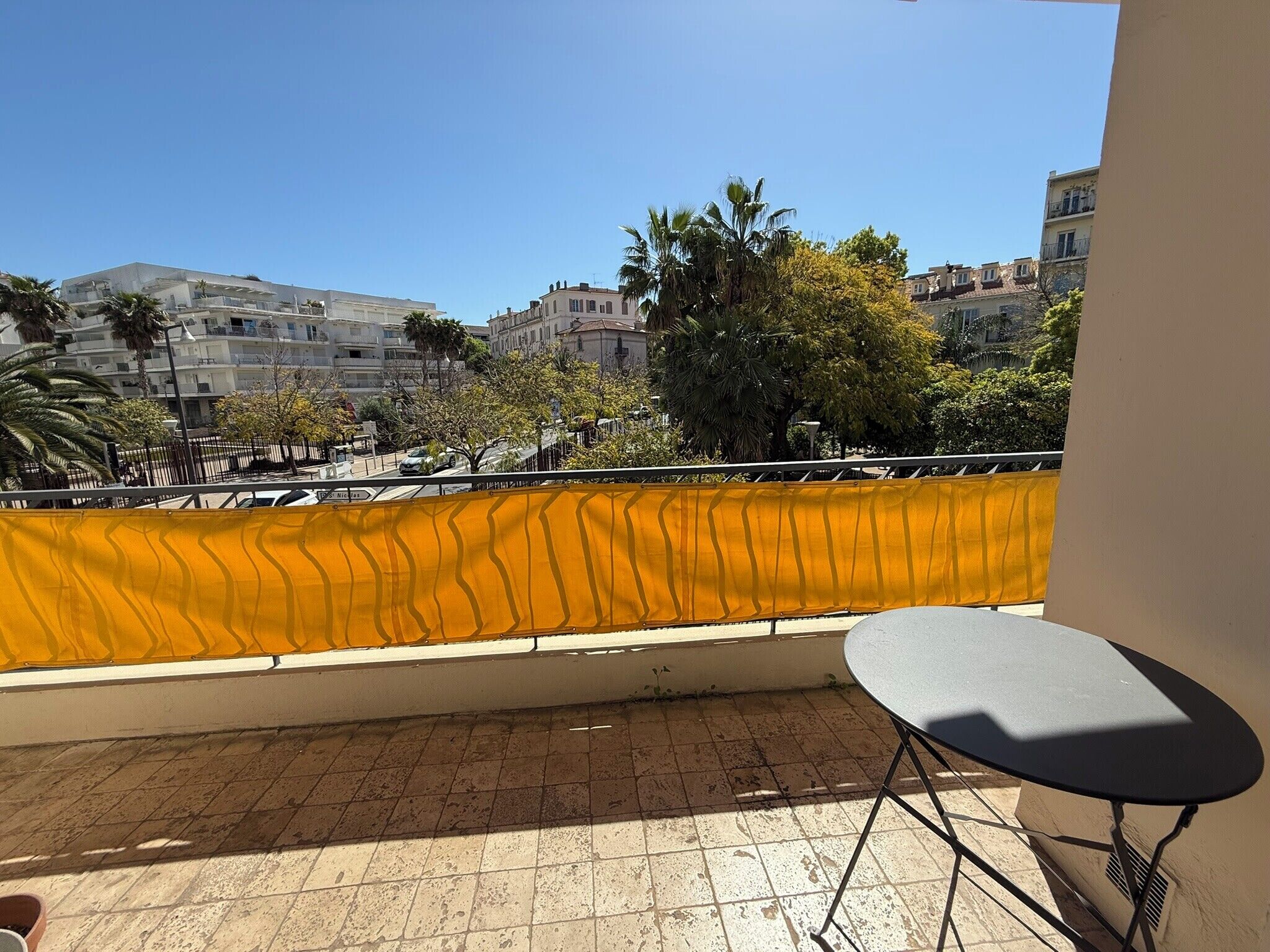 A balcony with a view of a cityscape, a yellow safety barrier, and a table.