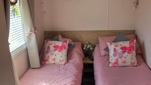A compact room with two beds, each with pink bedding and butterfly-patterned pillows, a wooden headboard, and a small table with a vase of flowers. - D&T Caravan Hire Southview Holiday Park Skegness (Skegness)