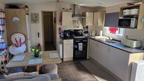 A compact kitchen with a stove, microwave, and sink. There is a dining area with a table and chairs. - D&T Caravan Hire Southview Holiday Park Skegness (Skegness)