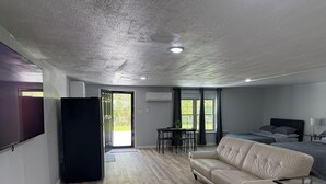 A modern room with a sofa, a bed, a dining table with chairs, and a refrigerator. - Modern Open Studio - 3 Beds - 2 queens & 1–Full Sleeps 6- Near Local Attractions (Marksville)