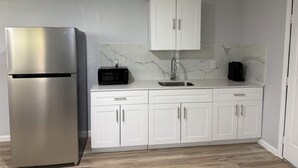 A kitchen with a stainless steel refrigerator, white cabinets, a marble backsplash, and a wooden floor. - Modern Open Studio - 3 Beds - 2 queens & 1–Full Sleeps 6- Near Local Attractions (Marksville)