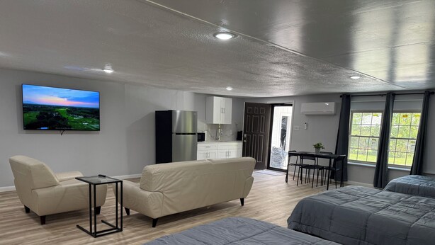 A modern hotel room with a sofa, two beds, a TV, a kitchen area, and a view of the outdoors. - Modern Open Studio - 3 Beds - 2 queens & 1–Full Sleeps 6- Near Local Attractions (Marksville)