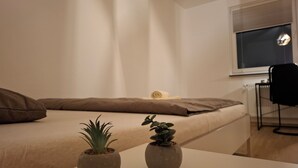 A bedroom with a bed, pillows, a window, a radiator, and two potted plants. - Room "white" in shared flat - central & quiet - VW, Autostadt, VfL parking lot and WLAN (Wolfsburg)