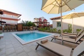 Ein Schwimmbecken mit Liegestühlen und Sonnenschirmen, umgeben von Gebäuden.