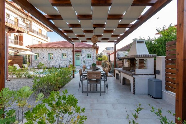 Eine Terrasse im Freien mit Tisch, Stühlen, einem Grill und einem Steinhaus im Hintergrund.