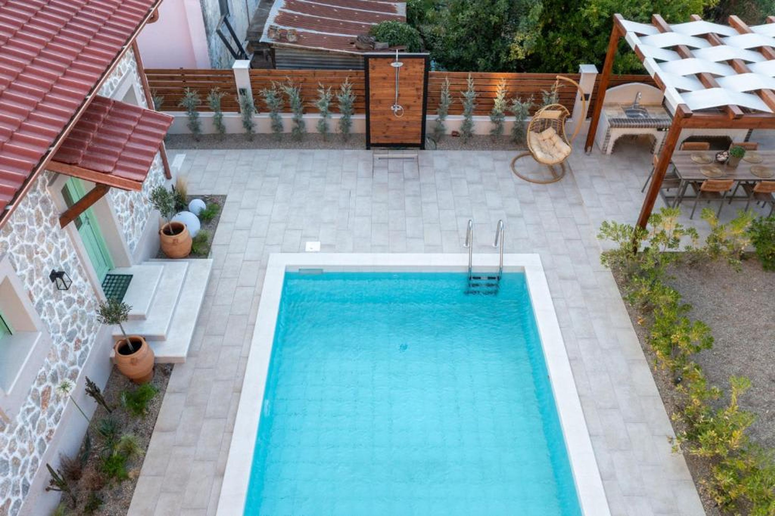 Una piscina amb un tramat de fusta, una pèrgola i mobles d'exterior.