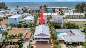 A coastal hotel with a prominent building highlighted by a red arrow, surrounded by other buildings and palm trees. - Coastal 2BR Duplex – Near Beach, Parks, Dining & Free Trolley (Bradenton Beach)
