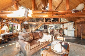 A spacious living area with a leather sofa, wooden ceiling beams, and a kitchen in the background.