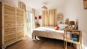 A bedroom with a bed, a wooden wardrobe, a bedside table with a lamp, and a window with curtains. - Magnificent house close to the beach (Perpignan)