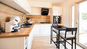 A compact kitchen with a coffee maker, a stove, and a dining area with a table and chairs. - Magnificent house close to the beach (Perpignan)