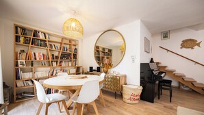 A room with a round table, white chairs, a bookshelf, a mirror, a piano, and a staircase. - Magnificent house close to the beach (Perpignan)
