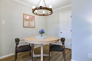 Ein Essbereich mit einem runden Tisch, vier Stühlen, einer Kristallleuchter und einem floralen Bild im Rahmen an der Wand.
