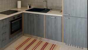 Una cucina moderna con mobili grigi, forno integrato, finestra sopra il lavello e un tappeto a righe sul pavimento.