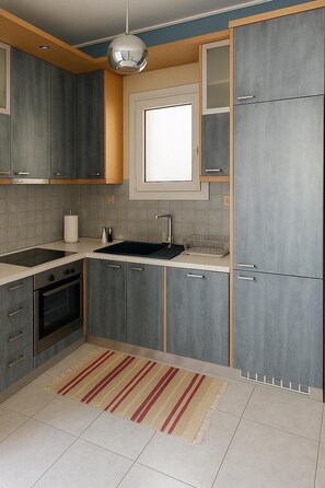 A modern kitchen with grey cabinets, a built-in oven, a window above the sink, and a striped rug on the floor. - Navarinou Kalamata Pearl Cozy Seaside apartment (Kalamata)