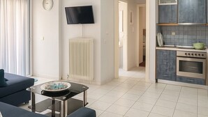 Un soggiorno moderno con divano, tavolino, televisore e angolo cottura con piano cottura e pensili.
