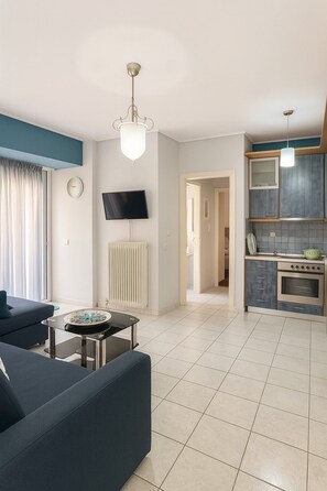 A modern living room with a sofa, a coffee table, a TV, and a kitchen area with a stove and cabinets. - Navarinou Kalamata Pearl Cozy Seaside apartment (Kalamata)