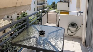 Un balcone con un tavolo e sedie in vetro, un tubo da giardino e vista sul mare e sugli edifici.