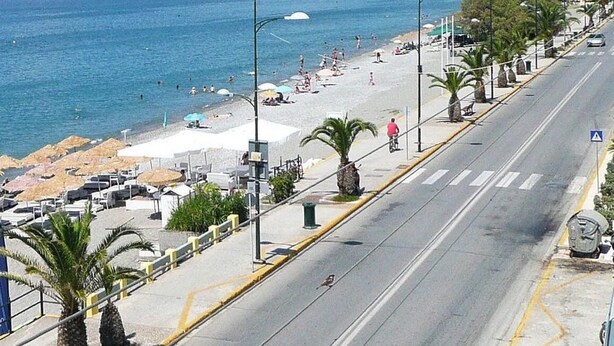 Una strada costiera con spiaggia, palme e cielo sereno.