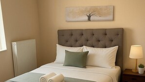 Un letto rifatto con un comò grigio, una lampada da comodino e un termosifone sulla parete.