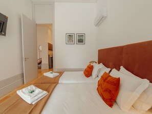 Ein Hotelzimmer mit zwei Betten, einem braunen Kopfteil, weißer Bettwäsche und zwei gerahmten Bildern an der Wand.
