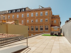 Ein Innenhof mit Fliesenboden, einem Metallgeländer und einem Gebäude mit zahlreichen Fenstern und Balkonen.