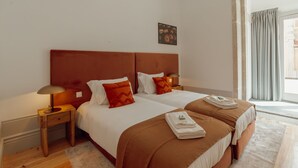 Una camera d'albergo con due letti, un comodino, una lampada, un quadro appeso e una finestra con tende.