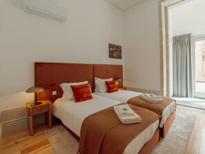Ein Hotelzimmer mit zwei Betten, einem Nachttisch, einer Lampe, einem Bild an der Wand und einem Fenster mit Vorhängen.
