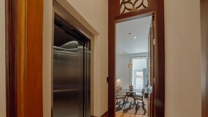 Un corridoio con una porta in legno che dà sull'ascensore, un'area pranzo con tavolo e sedie, e vista su un balcone.