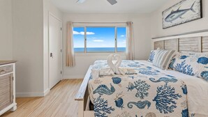 Un dormitorio con cama, ventilador de techo, ventana con vistas y un cuadro en la pared.