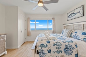 A bedroom with a bed, a ceiling fan, a window with a view, and a painting on the wall. - Pinnacle Port, C2-603 (Panama City Beach)