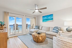 A living room with a sofa, a coffee table, a ceiling fan, a painting, and a view through a sliding door. - Pinnacle Port, C2-603 (Panama City Beach)