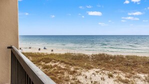 Uitzicht op een strand vanaf een balkon, met heldere lucht, zandstrand en schaarse begroeiing.