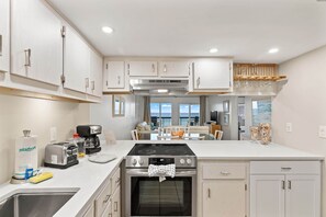 A modern kitchen with a stove, oven, and built-in appliances. There is a dining area with a table and chairs. - Pinnacle Port, C2-301 (Panama City Beach)